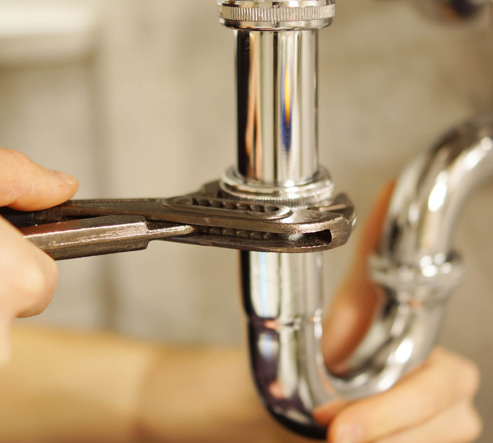 Plumbing repair service. Professional installer with spanner checking pipe.